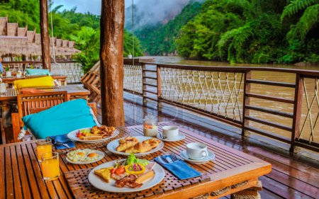 Foto de Mesa de desayuno en una casa de playa tropical en el río Kwai en Tailandia.Casa balsa flotante de madera en el río Kwai Kanchanaburi, Tailandia, desayuno con huevos pan y café - Imagen libre de derechos