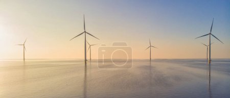 Photo for Windmill park in the ocean at sunset, drone aerial view of windmill turbines generating green energy, windmills isolated at sea in the Netherlands. - Royalty Free Image