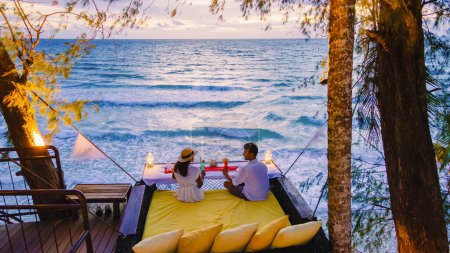 Téléchargez les photos : Dîner romantique sur la plage à Koh Kood en Thaïlande, un couple d'hommes et de femmes dînant sur la plage haut dans l'arbre à un nid d'oiseaux en Thaïlande pendant le coucher du soleil - en image libre de droit
