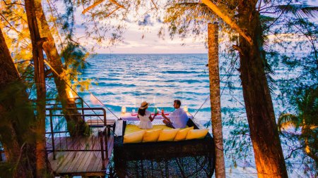 Téléchargez les photos : Dîner romantique sur la plage à Koh Kood en Thaïlande, un couple d'hommes et de femmes dînant sur la plage haut dans l'arbre à un nid d'oiseaux en Thaïlande pendant le coucher du soleil - en image libre de droit