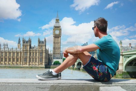 Photo for A young men tourist on a city trip in London looking at Big Ben at Westminster Bridge, a young man by the river Thames at the famous places in London, Big Ben and Westminster Bridge in London UK - Royalty Free Image