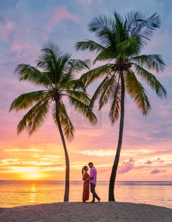Téléchargez les photos : Couple sur la plage avec des palmiers regardant coucher de soleil à la plage tropicale de Sainte-Lucie ou Sainte-Lucie Caraïbes. hommes et femmes en vacances à Sainte-Lucie une île tropicale avec des palmiers regardant le coucher du soleil - en image libre de droit