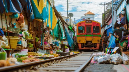Maeklong Eisenbahnmarkt Thailand, Zug auf Schiene, der sich langsam bewegt. Regenschirm-Frischemarkt auf dem Bahngleis, Mae Klong Bahnhof, Bangkok, ein berühmter Eisenbahnmarkt in Thailand