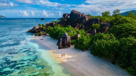 Foto de Anse Source dArgent beach, La Digue Island, Seychelles, pareja de hombres y mujeres caminando por la playa al atardecer en unas vacaciones de lujo en las Seychelles - Imagen libre de derechos