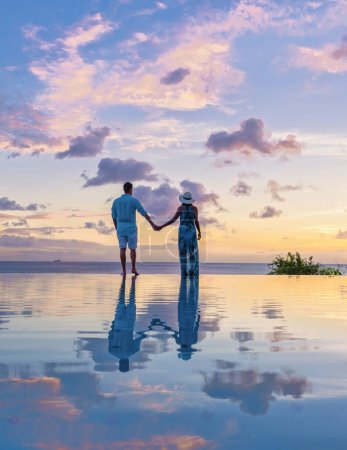 Photo for Young men and women watching the sunset with reflection in the infinity swimming pool at Saint Lucia Caribbean, couple at infinity pool during sunset on a luxury vacation at St Lucia - Royalty Free Image