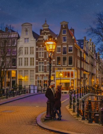 Téléchargez les photos : Amsterdam canaux le soir, un couple d'hommes et de femmes en voyage à Amsterdam pendant les vacances de Noël - en image libre de droit