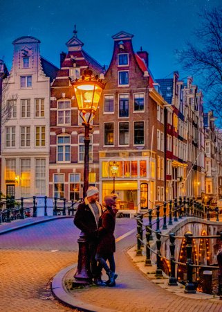 Photo for Amsterdam canals in the evening during Christmas, a couple of men and women on a city trip in Amsterdam in the Netherlands during winter. old city street with street lanterns in the evening - Royalty Free Image
