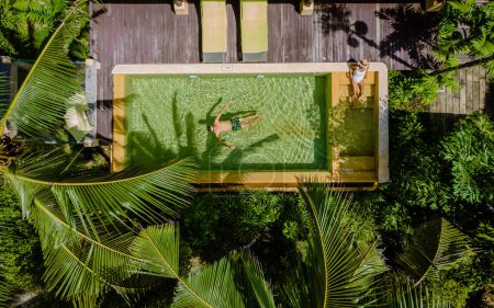 Téléchargez les photos : Maison moderne avec piscine, villa piscine moderne à la plage, villa de luxe en Thaïlande, un couple d'hommes et de femmes en vacances de luxe en Thaïlande se détendre dans la piscine d'une villa piscine - en image libre de droit