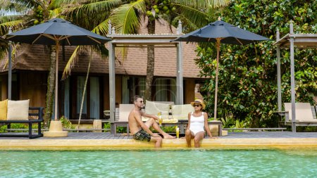 Téléchargez les photos : Un couple d'hommes et de femmes en vacances de luxe en Thaïlande se détendre dans la piscine d'un complexe de luxe sur la plage de Koh Kood - en image libre de droit