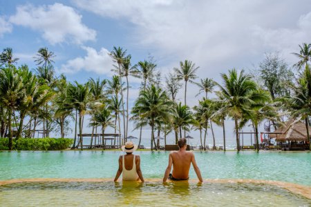 Téléchargez les photos : Un couple d'hommes et de femmes en vacances de luxe en Thaïlande se détendre dans la piscine d'un complexe de luxe sur la plage de Koh Kood - en image libre de droit