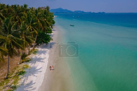 Téléchargez les photos : Un couple d'hommes et de femmes en vacances à Koh Mook île tropicale dans la mer d'Andaman en Thaïlande, hommes et femmes marchant sur une plage avec des palmiers - en image libre de droit