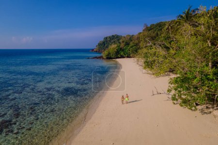 Téléchargez les photos : Un couple d'hommes et de femmes en vacances à Koh Mook île tropicale dans la mer d'Andaman en Thaïlande, hommes et femmes marchant sur une plage avec des palmiers par une journée ensoleillée - en image libre de droit