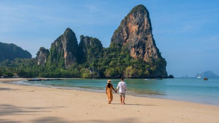 Foto de Un par de hombres y mujeres caminando por la playa de Railay Beach Krabi Tailandia, la playa tropical de Railay Krabi, una diversa pareja multirracial caminando de la mano juntos en la playa - Imagen libre de derechos