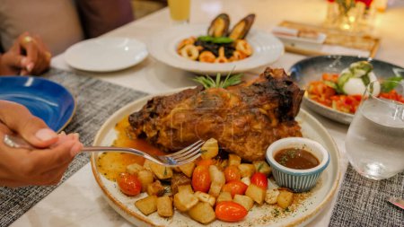 Téléchargez les photos : Dîner dans un restaurant italien en Thaïlande, porc cuit lentement, épaule rôtie entière de porc effiloché avec une riche marinade chaude épicée sur une table avec du chili, de l'ail et du romarin. vue d'en haut, gros plan - en image libre de droit