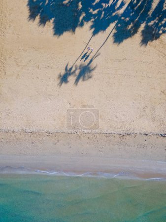 Photo for Drone view from above at a couple of men and women walking on the beach with palm trees on the beach road of Pattaya Thailand, shadow of palm tree in the sand on the beach - Royalty Free Image