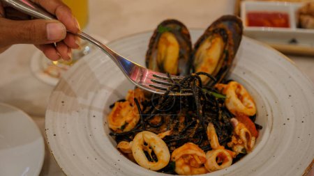 Foto de Espaguetis de tinta de calamar negro en un plato con tenedor y cena de mariscos en un restaurante italiano en Tailandia - Imagen libre de derechos