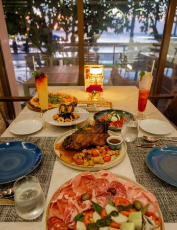 Photo for Dinner table in an Italian restaurant in Thailand, antipasti with roasted pork and pizza - Royalty Free Image