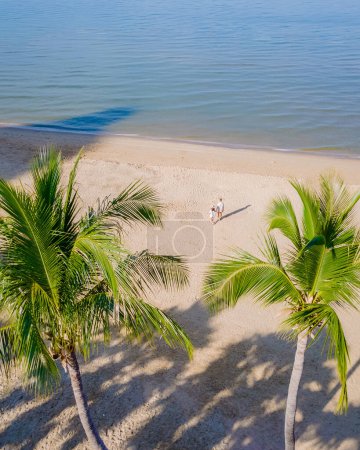 Téléchargez les photos : Un couple d'hommes et de femmes marchant sur la plage de Pattaya avec des palmiers, vue de drone d'en haut à la plage avec des palmiers et des ombres dans le sable de la plage de Pattaya Thaïlande - en image libre de droit