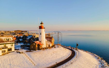 Photo for Sunset at the lighthouse and harbor of Urk Holland. Fishing village Urk. Beautiful sunset during the evening in winter weather with a snow covered lighthouse - Royalty Free Image
