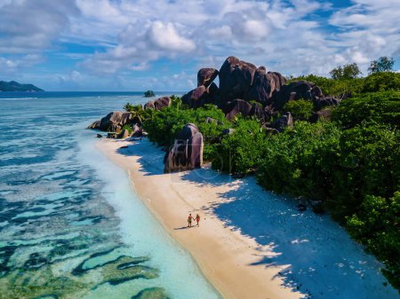 Téléchargez les photos : Anse Source d'Argent plage, Île La Digue, Seychelles, couple hommes et femmes marchant sur la plage au coucher du soleil lors de vacances de luxe - en image libre de droit