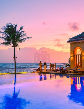 Téléchargez les photos : Un jeune couple d'hommes et de femmes dans une piscine pendant des vacances sur une île tropicale regardant le coucher du soleil sur une plage tropicale, un couple en lune de miel - en image libre de droit