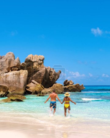 Foto de Playa de Anse Cocos La Digue Island, Seychelles, pareja multiétnica mixta diversa Hombres caucásicos y mujeres asiáticas caminando por la playa durante la puesta del sol en unas vacaciones de lujo - Imagen libre de derechos