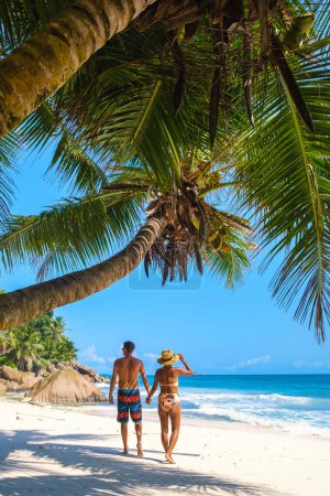 Téléchargez les photos : Anse Patates, La Digue Seychelles, un jeune couple d'hommes et de femmes sur une plage tropicale pendant des vacances de luxe aux Seychelles. Plage tropicale Anse Patates, La Digue Seychelles pendant les vacances d'été - en image libre de droit