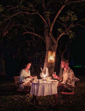 Téléchargez les photos : Afrique du Sud Kwazulu Natal, un lodge de safari de luxe dans la brousse d'une réserve de gibier, un couple d'hommes et une femme asiatique dînant aux chandelles le soir - en image libre de droit