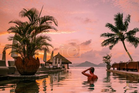 Photo for Young men in a swimming pool during sunset, a Luxury swimming pool in a tropical resort, and relaxing holidays in the Seychelles islands. La Digue, a Young guy during sunset by the swimming pool - Royalty Free Image