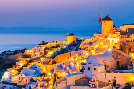 Téléchargez les photos : Églises blanches un dôme bleu près de l'océan d'Oia Santorin Grèce pendant le coucher du soleil dans le crépuscule du soir - en image libre de droit