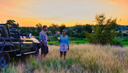 Téléchargez les photos : Femmes asiatiques et hommes européens en safari dans le parc national Kruger en Afrique du Sud. Deux hommes et deux femmes en safari. Touristes dans une jeep à la recherche coucher de soleil avec des boissons sur safari à un coucher de soleil - en image libre de droit