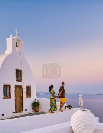 Foto de Hombres y mujeres visitan el pueblo griego encalado de Oia Santorini, una pareja que observa el amanecer en Santorini durante las vacaciones - Imagen libre de derechos