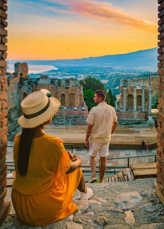 Téléchargez les photos : Taormina Sicile, couple regardant le coucher du soleil sur les ruines du théâtre grec antique à Taormina, en Sicile. couple d'âge moyen en vacances en Sicile pendant les vacances d'été - en image libre de droit