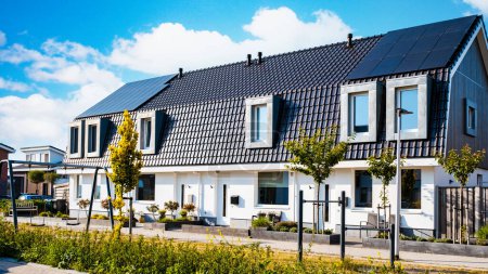 Téléchargez les photos : Maisons nouvellement construites avec des panneaux solaires fixés sur le toit contre un ciel ensoleillé, Gros plan du nouveau bâtiment avec des panneaux solaires noirs aux Pays-Bas - en image libre de droit
