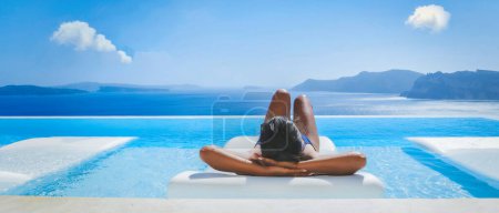 Foto de Mujeres asiáticas jóvenes de vacaciones en Santorini relajándose en una piscina con vistas al océano Caldera de Santorini, piscina Infinity en Oia Grecia, islas griegas Egeo Cícladas. - Imagen libre de derechos