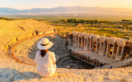 Foto de Hierapolis antigua ciudad Pamukkale Turquía, una mujer joven con un sombrero viendo la puesta de sol por las ruinas Patrimonio de la Unesco. Mujeres asiáticas viendo la puesta de sol en el antiguo Anfiteatro en Turquía - Imagen libre de derechos