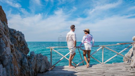 Photo for A couple of European men and an Asian woman looking at a blue ocean from a wooden pier jetty at Ko Kham Island Chonburi Samaesan Thailand, a couple at a tropical island with turqouse colored ocen - Royalty Free Image