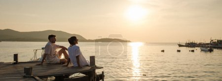 Téléchargez les photos : Un couple d'hommes européens et une femme asiatique en vacances en Thaïlande, couple regardant le coucher de soleil assis sur une jetée de pont en bois dans l'océan en Thaïlande samésienne - en image libre de droit