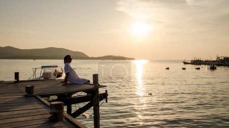 Téléchargez les photos : Femme asiatique regardant le coucher du soleil sur une jetée en bois dans l'océan pendant le coucher du soleil en Thaïlande samésienne - en image libre de droit