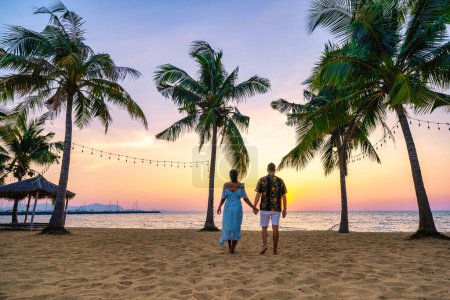 Foto de Playa Najomtien Pattaya Tailandia, puesta de sol en una playa tropical con palmeras. Pattaya Tailandia. Una pareja de hombres y una mujer de mediana edad observando la puesta de sol en la playa con palmeras en la playa de Na Jomtien - Imagen libre de derechos