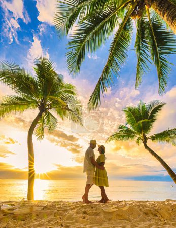 Foto de Un par de hombres y mujeres abrazándose y besándose en la playa durante el atardecer en Phuket durante las vacaciones, una playa con arena blanca y palmeras Bang Tao Beach Phuket Tailandia. - Imagen libre de derechos