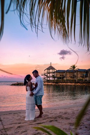 Foto de Resort de lujo tropical Curazao con playa privada y palmeras, vacaciones de lujo Curazao Caribe, pareja de hombres y mujeres viendo la puesta de sol en la playa con piscina y palmeras - Imagen libre de derechos