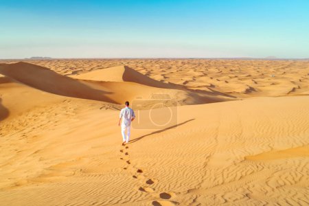Foto de Dunas de arena del desierto de Dubái, hombres jóvenes caminando en las dunas de arena de Dubái durante un safari por el desierto. hombre caminando en el desierto de Dubai - Imagen libre de derechos
