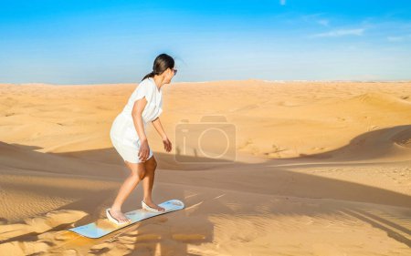 Young women sand surfing at the sand dunes of Dubai United Arab Emirates, sand desert on a sunny day in Dubai. Tourist on a desert safari in Dubai