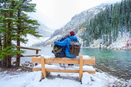 Lake Agnes by Lake Louise Banff National Park with snowy mountains in the Canadian Rocky Mountains during winter. A young couple of men and women sitting on a bench by the lake in Canada with snow