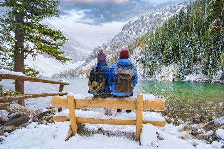 Téléchargez les photos : Lac Agnes près du parc national Banff de Lake Louise avec des montagnes enneigées dans les montagnes Rocheuses canadiennes pendant l'hiver. Deux hommes et deux femmes assis sur un banc au bord du lac vert émeraude au Canada avec - en image libre de droit