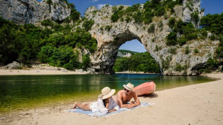 Photo for Couple on vacation in the Ardeche France Pont d Arc Ardeche, view of Natural arch in Vallon Pont dArc in Ardeche canyon in France Europe Rhone Alps Dordogne, men and woman at the beach by the river - Royalty Free Image