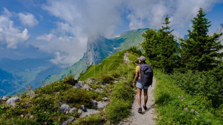 Téléchargez les photos : Randonnées pédestres dans les Alpes suisses pendant les vacances d'été avec un sac à dos et des bottes de randonnée. femme marchant sur le sentier Saxer Lucke en Suisse pendant l'été - en image libre de droit