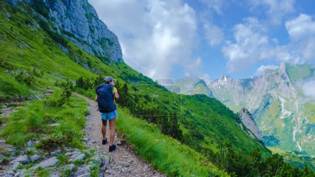 Téléchargez les photos : Une femme asiatique qui fait de la randonnée dans les Alpes suisses pendant les vacances d'été avec un sac à dos et des bottes de randonnée. femme marchant sur le sentier Saxer Lucke en Suisse pendant l'été - en image libre de droit