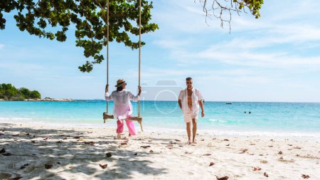 Foto de Un par de hombres y mujeres en un columpio en la playa de Koh Samet Island Tailandia, playa tropical en Samed Island con un océano de color turquesa. Mujeres asiáticas y hombres europeos de vacaciones en Tailandia - Imagen libre de derechos